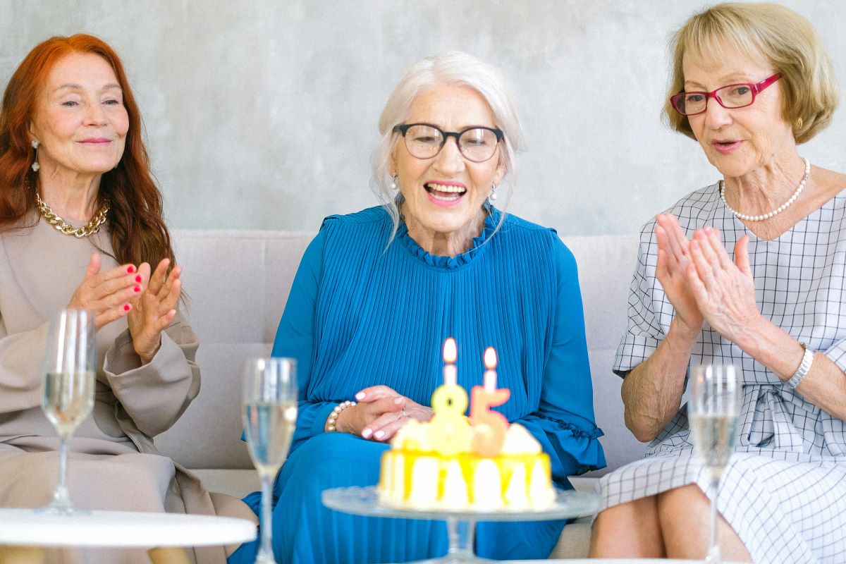 Three elderly women celebrating a birthday with a cake, representing longevity and happiness.