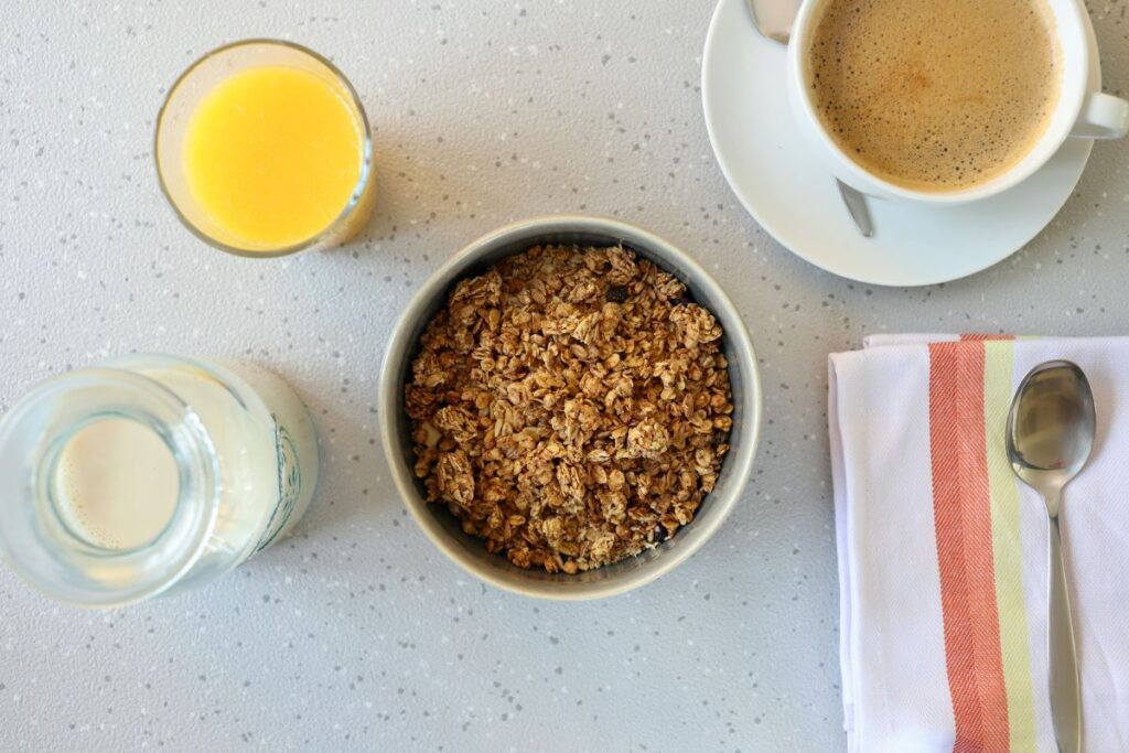 A healthy breakfast bowl with granola, a glass of orange juice, and a cup of coffee on a clean table.